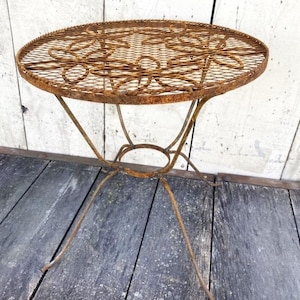 May include: A rusty metal garden table with a round, decorative top and a simple, three-legged base.