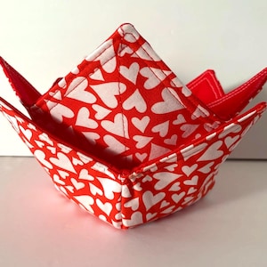 May include: Two fabric bowl cozies, one nested inside the other. The cozies are red with a white heart pattern. The interior and the edges are solid red. These are designed to be used in the microwave.