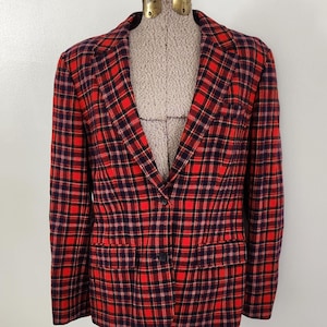 May include: A red and black plaid blazer displayed on a mannequin. The blazer has a classic notched collar, a single-button closure, and two front pockets. The plaid pattern features a bold red base with black and purple intersecting lines.