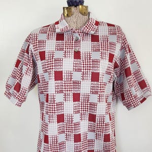 May include: A short-sleeved shirt with a patchwork design in shades of red, gray, and white. The shirt has a collared neckline and a button-down front. The fabric appears to be a lightweight material.