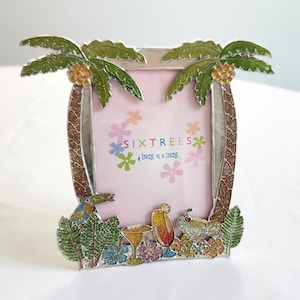 May include: A rectangular metal picture frame featuring a tropical theme with two palm trees at the top, a toucan, and colorful cocktail glasses at the base. The frame includes a pink insert with the text SIXTREES 4 inch x 6 inch and floral accents.