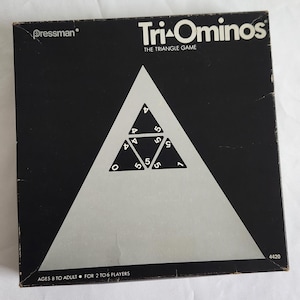 May include: A black box game with the title "Tri-Ominos: The Triangle Game" and the Pressman logo. The box features a white triangle with numbers and a silver background.