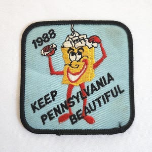 May include: A vintage patch with a cartoon character holding up its arms. The character is yellow with a smiling face and red arms and feet. The patch reads "KEEP PENNSYLVANIA BEAUTIFUL" and "1988" on a light blue background.