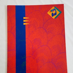 May include: Red notebook with a blue stripe down the side and a yellow, green, and blue toucan design in the top right corner.