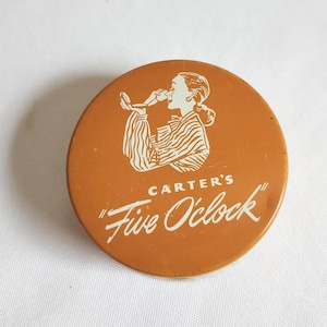 May include: A round, orange-brown button with the text "CARTER'S" and "Five O'clock" in white script. The button features a white illustration of a person drinking from a cup. The person is wearing a striped garment.
