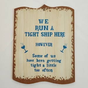 May include: Wooden sign with a distressed finish, featuring the text "WE RUN A TIGHT SHIP HERE HOWEVER Some of us have been getting tight a little too often" in blue. Two cocktail glass icons flank the text.
