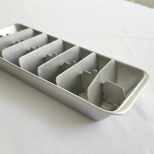 May include: A silver metal ice cube tray with six compartments for making ice cubes.