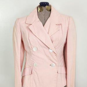 May include: A light pink double-breasted blazer with a plaid pattern. The blazer has two rows of white buttons, two front pockets, and a notched collar. The jacket is displayed on a mannequin.