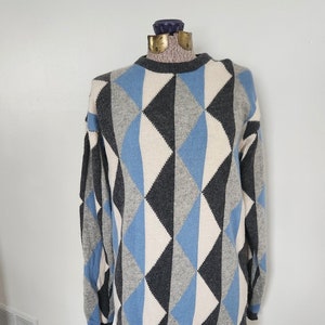 May include: A long-sleeved sweater with a geometric pattern in shades of blue, gray, and white. The sweater has a crew neck and a relaxed fit.