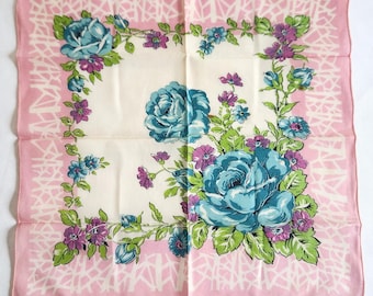 May include: A square, vintage pink scarf with a white center featuring large teal roses and smaller purple and blue flowers. The pink border has a white, abstract design.