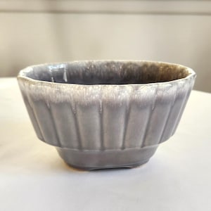 May include: A small, gray ceramic planter with a white glaze and a fluted design. The planter is perfect for small plants or succulents.