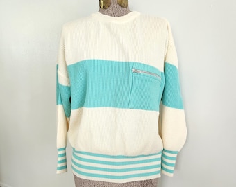 May include: A white and turquoise striped sweater with a zippered pocket on the front. The sweater has a ribbed texture and a white trim around the bottom and sleeves.