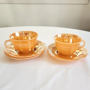 May include: Two vintage peach-colored teacups and saucers. The cups and saucers have a delicate, rippled design.