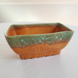 May include: A rectangular ceramic planter with a scalloped base. The planter is glazed in shades of brown and green.