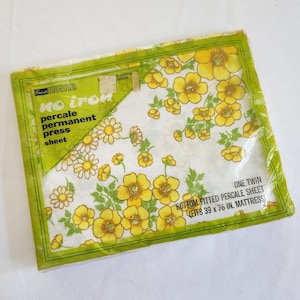 May include: Sealed package of a twin-size percale sheet with a floral pattern. The sheet features yellow flowers and green leaves on a white background. The packaging reads "No Iron" and "Permanent Press".