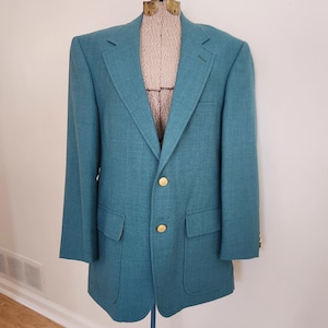 May include: A teal blazer with gold buttons. The blazer has a single breasted closure and a patch pocket on the left side.