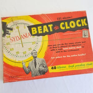 May include: Vintage "Beat the Clock" board game box with a red and yellow design. The box features a clock face, the text "SYLVANIA", and an image of a man. The text "CBS television's" is also visible.
