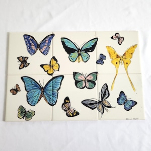 May include: A rectangular wall art piece composed of six square tiles featuring a collection of hand-painted butterflies in various sizes and colors, including shades of blue, yellow, green, and black, set against a cream-colored background.