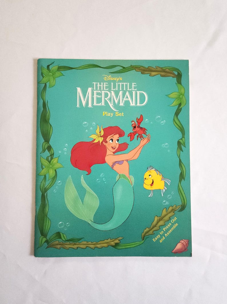 Puede incluir: Un set de juego de Disney La Sirenita con Ariel, Sebasti&aacute;n y Flounder sobre un fondo verde azulado. La portada incluye bordes de algas verdes, burbujas y el texto 'Disney's THE LITTLE MERMAID Play Set' y 'Easy to Press Out and Assemble'.