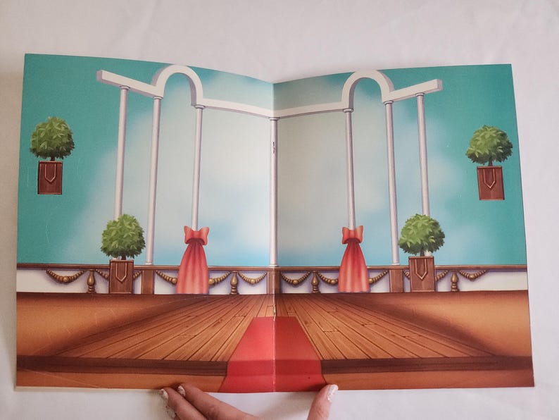 Puede incluir: Un tel&oacute;n de fondo de papel impreso que muestra una escena de sal&oacute;n de baile con suelo de madera, una alfombra roja central, columnas arquitect&oacute;nicas blancas y plantas verdes. La escena incluye cortinas rojas y un cielo azul claro.