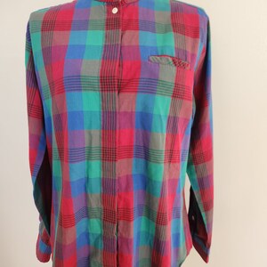 May include: A long-sleeved button-up shirt with a plaid pattern in shades of red, green, blue, and purple. The shirt has a mandarin collar and a single button closure at the neck.