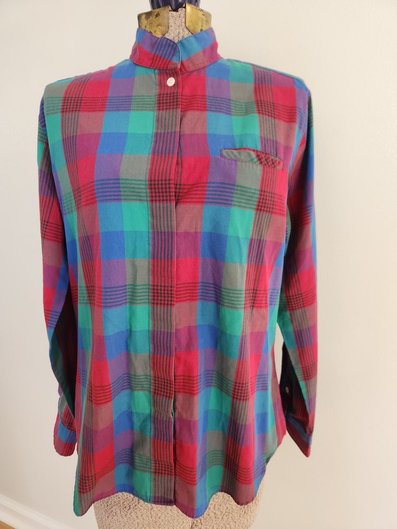 May include: A long-sleeved button-up shirt with a plaid pattern in shades of red, green, blue, and purple. The shirt has a mandarin collar and a single button closure at the neck.