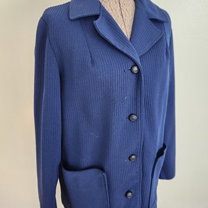 May include: A navy blue ribbed knit jacket with a collar, four black buttons, and a patch pocket on the left side.