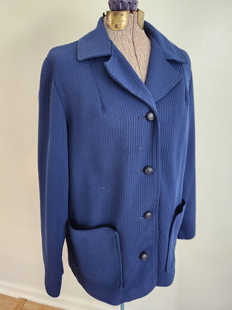 May include: A navy blue ribbed knit jacket with a collar, four black buttons, and a patch pocket on the left side.