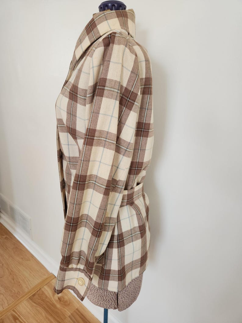 May include: A beige and brown plaid jacket with a matching belt. The jacket has a collared neckline and buttoned cuffs. The plaid pattern includes light blue lines. The jacket is displayed on a mannequin.