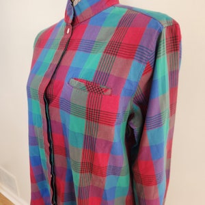 May include: A long-sleeved button-down shirt with a plaid pattern in shades of red, green, blue, and purple. The shirt has a mandarin collar and a single chest pocket.