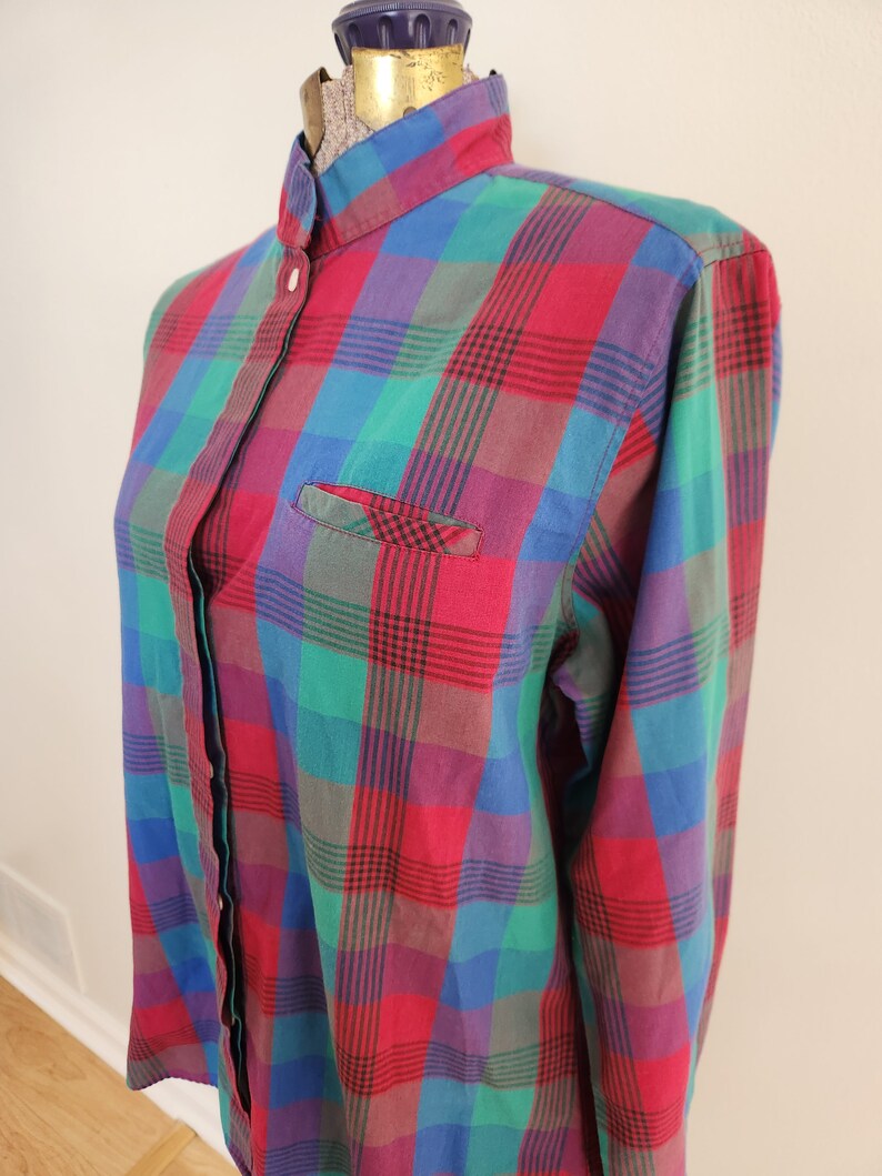 May include: A long-sleeved button-down shirt with a plaid pattern in shades of red, green, blue, and purple. The shirt has a mandarin collar and a single chest pocket.