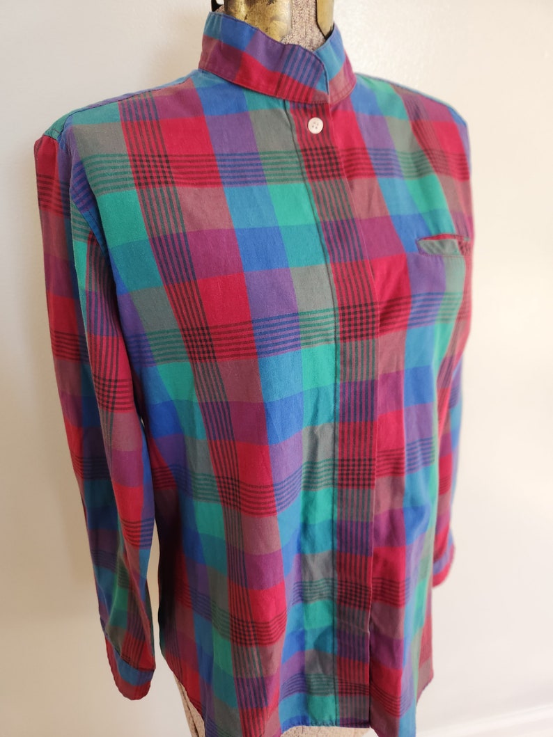 May include: A long-sleeved plaid shirt with a mandarin collar and button closure. The shirt is red, green, blue, and purple.