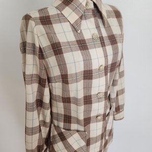 May include: A vintage plaid jacket in cream, brown, and light blue. The jacket features a collared neckline, button-down front, long sleeves, and two front pockets. The plaid pattern is a classic design.