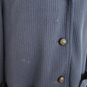 May include: A dark blue ribbed cardigan with three black buttons. The cardigan has two pockets on the front.