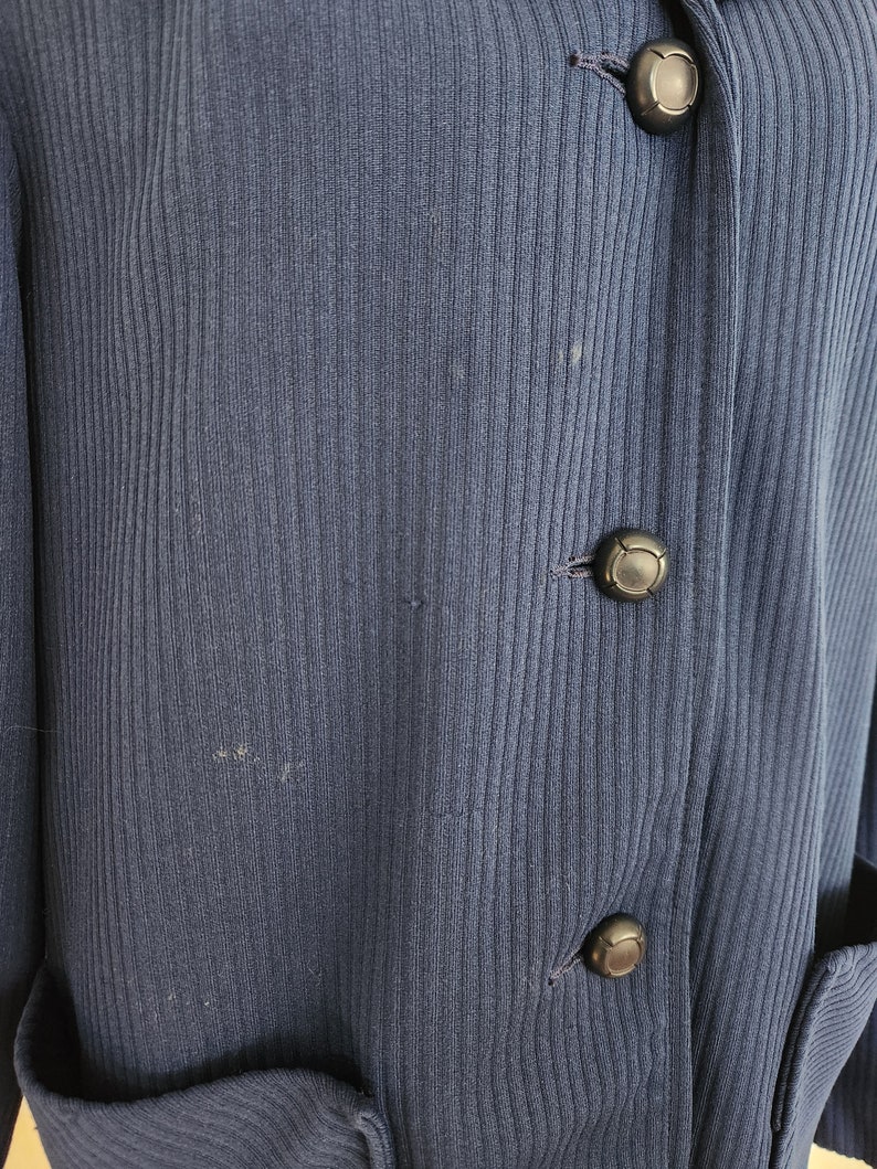 May include: A dark blue ribbed cardigan with three black buttons. The cardigan has two pockets on the front.