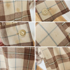 May include: Close-up of a tan, brown, and light blue plaid blazer. The blazer has a button closure and a button on the sleeve. The fabric has a woven texture. The blazer appears to be vintage.