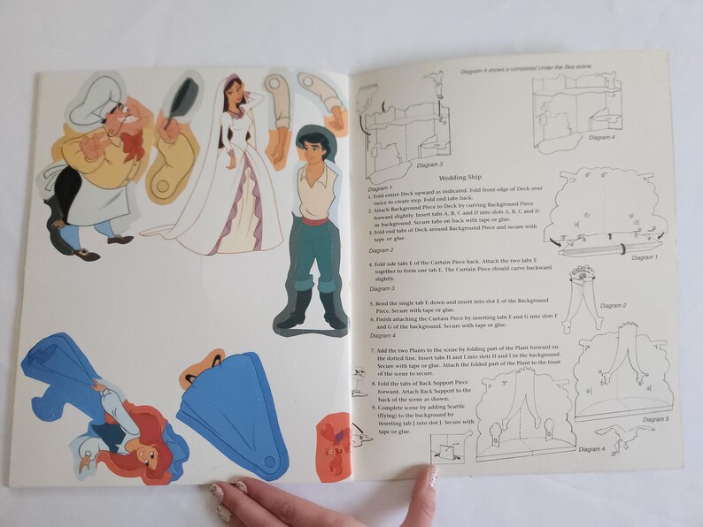 Puede incluir: Una p&aacute;gina de libro de manualidades de papel con personajes recortables que incluyen un chef, una novia con vestido blanco y un novio con camisa beige y pantalones verde azulado. La p&aacute;gina incluye instrucciones de montaje para un barco.