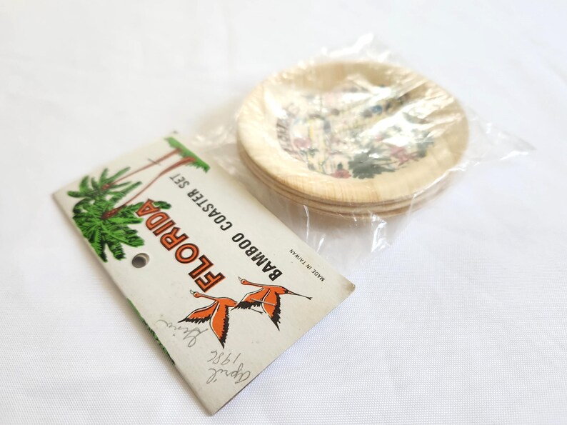 Puede incluir: Un juego de posavasos de bamb&uacute; con tem&aacute;tica de Florida. Los posavasos est&aacute;n en un paquete de pl&aacute;stico transparente. El embalaje incluye una etiqueta con las palabras "Florida Bamboo Coaster Set" e ilustraciones de palmeras y flamencos.