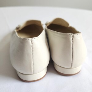 Puede incluir: Un par de mocasines de cuero color crema. Los zapatos tienen una punta redondeada, un tac&oacute;n bajo y un elemento decorativo en la parte superior. Las costuras son visibles a lo largo de la costura trasera. Las suelas son de color marr&oacute;n claro.