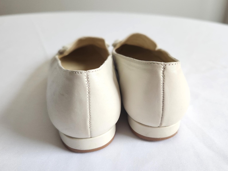 Puede incluir: Un par de mocasines de cuero color crema. Los zapatos tienen una punta redondeada, un tac&oacute;n bajo y un elemento decorativo en la parte superior. Las costuras son visibles a lo largo de la costura trasera. Las suelas son de color marr&oacute;n claro.