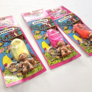 Puede incluir: Tres llaveros vintage de Troll Dolls en su embalaje original. Cada llavero presenta un mu&ntilde;eco troll marr&oacute;n con pelo colorido: amarillo, rosa y naranja. El embalaje es rosa y azul con las palabras "Troll Dolls" y "Keychain".