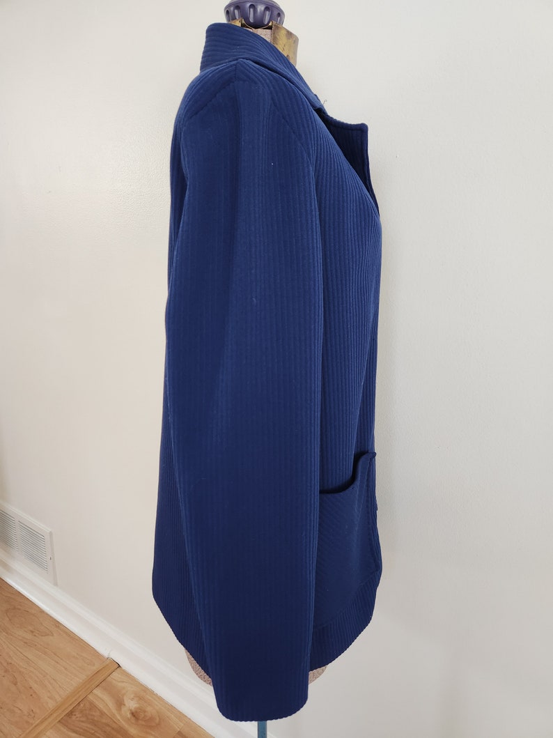 May include: A navy blue blazer with a single pocket on the right side. The blazer has a ribbed texture and a collar.