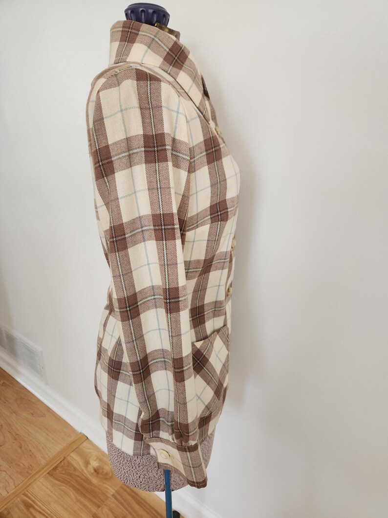 May include: A long-sleeved plaid shirt in cream, brown, and light blue. The shirt has a collared neckline, buttoned cuffs, and a single pocket. The fabric has a classic plaid pattern.