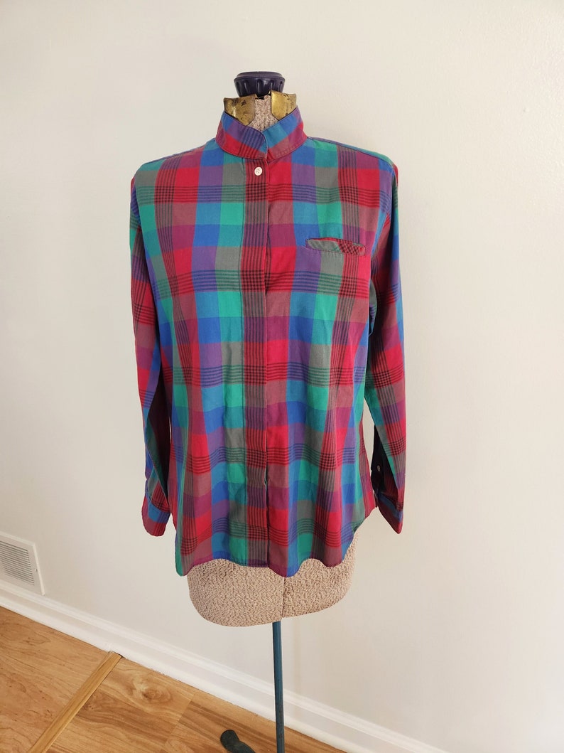 May include: A long-sleeved plaid shirt with a mandarin collar and button closure. The shirt is red, green, blue, and purple.