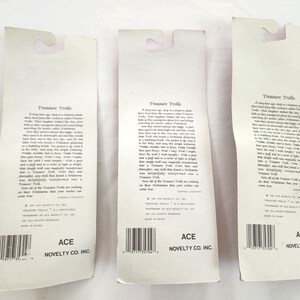 Puede incluir: Tres tarjetas de embalaje de juguetes vintage de Treasure Trolls. Cada tarjeta es blanca con una parte superior curvada y un c&oacute;digo de barras en la parte inferior. El texto "Treasure Trolls" est&aacute; impreso en la parte superior, con texto adicional debajo. La parte inferior de cada tarjeta dice "ACE NOVELTY CO. INC."