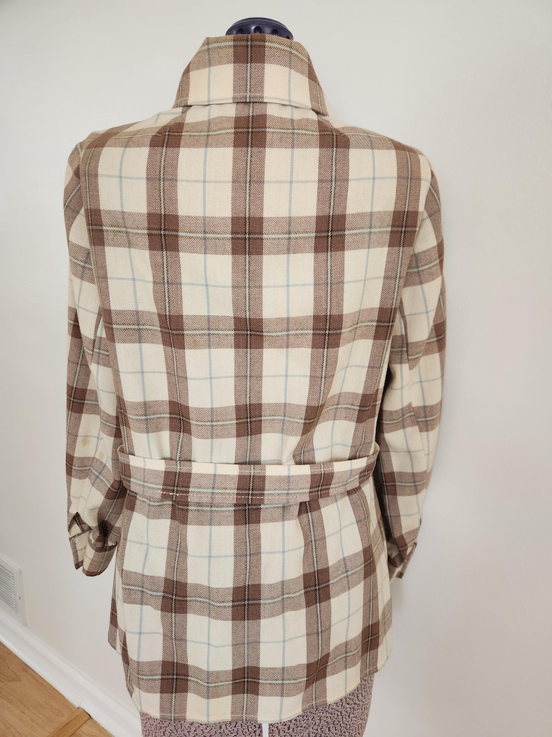 May include: A beige and brown plaid jacket with a matching belt. The jacket features a classic collar and long sleeves. The plaid pattern includes thin light blue lines. The jacket is displayed on a mannequin.