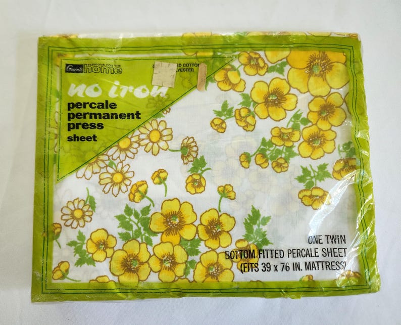 May include: A packaged twin-size percale sheet with a floral pattern. The sheet features yellow and white flowers with green leaves on a white background. The packaging is green with text that reads "no iron" and "bottom fitted percale sheet (fits 39 x 76 in. mattress)."