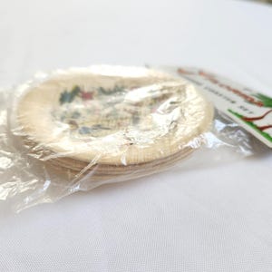 Puede incluir: Un juego de posavasos redondos con una imagen colorida, empaquetados en pl&aacute;stico transparente. Los posavasos parecen estar hechos de madera de color claro. Una etiqueta con texto y una ilustraci&oacute;n de palmera es visible.