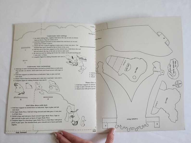 Puede incluir: Una hoja de instrucciones de papel con dibujos de l&iacute;neas negras y texto para ensamblar personajes de Disney. La p&aacute;gina incluye diagramas para Ariel bajo el agua, Ariel nadando, Ariel con vestido azul, el Pr&iacute;ncipe Eric y Max, con pesta&ntilde;as etiquetadas.