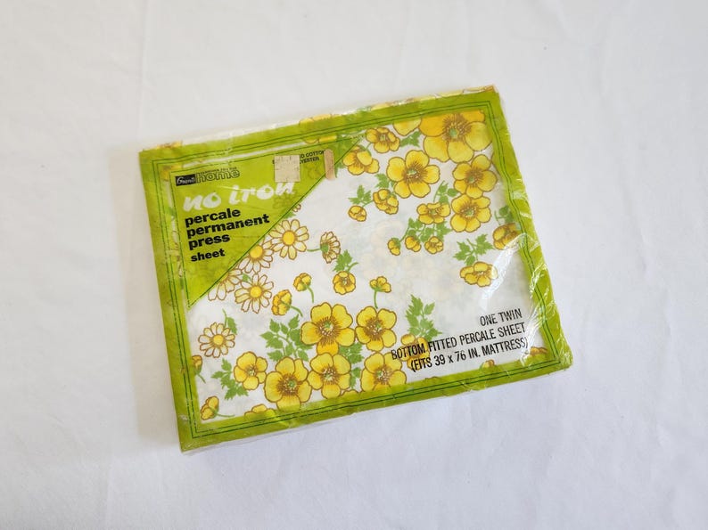 May include: Sealed package of a twin-size percale sheet with a floral pattern. The sheet features yellow flowers and green leaves on a white background. The packaging reads "No Iron" and "Permanent Press".
